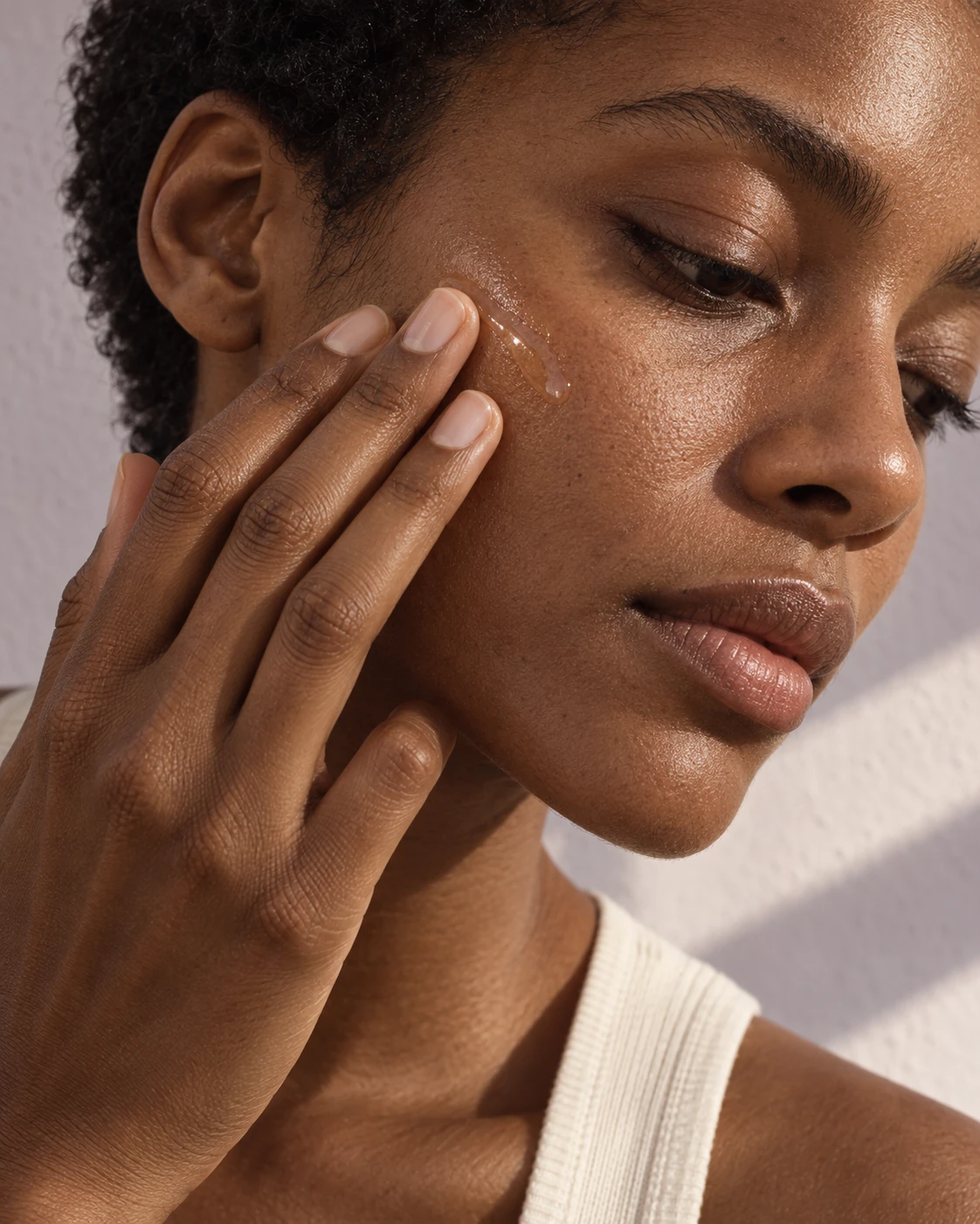 Close-up of a woman gently applying serum to her cheek, with natural skin texture visible